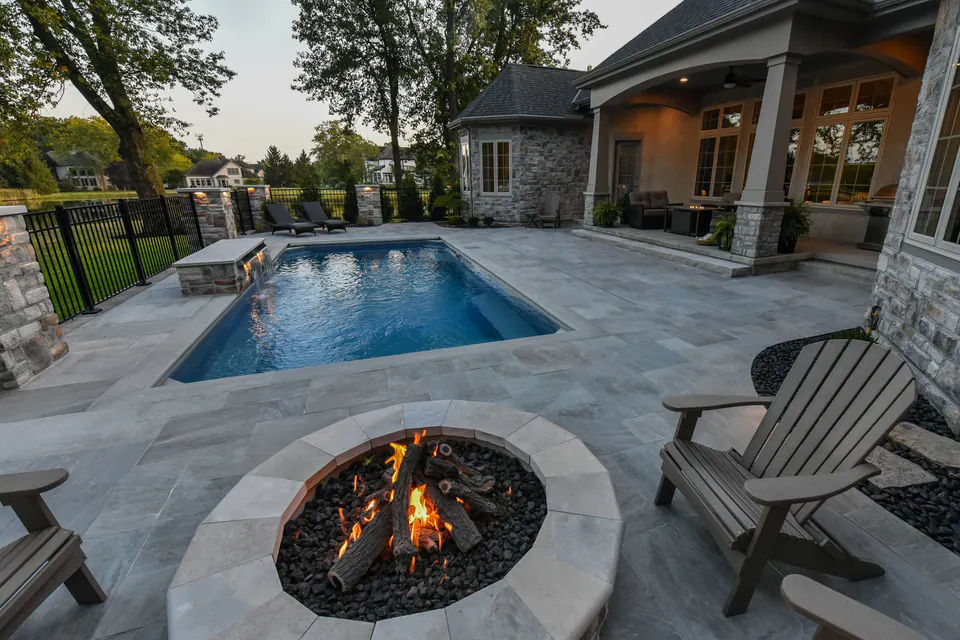 Bluestone pool patio with round gas firepit, limestone cap, ceramic gas logs, black metal fence, and lounge chairs